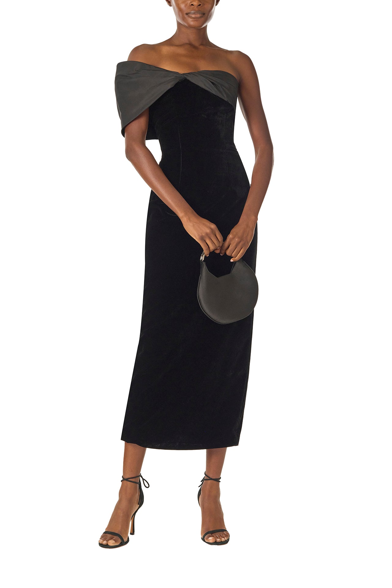 Monique Lhuillier Fall 2024 asymmetric, off the shoulder sheath dress in noir silk faille and velvet with draped twist detail at neckline - front with Demi bag.