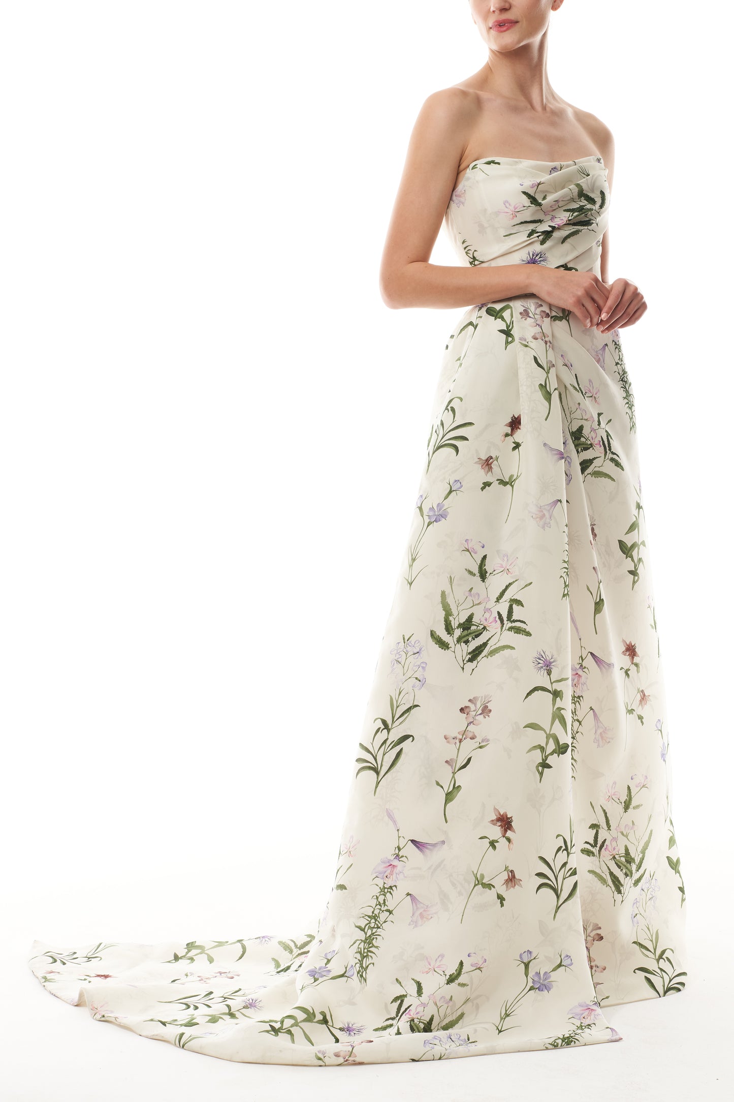Monique Lhuillier Fall 2025 strapless, floor length gown with draped bodice and high leg slit in ivory floral multi printed gazar fabric - side with train.