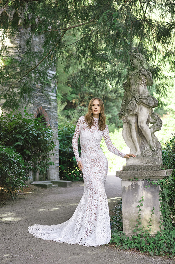 Woman wearing Monique Lhuillier Fall 2020 white fitted guipure lace Atherton gown with matching long sleeve high neck jacket