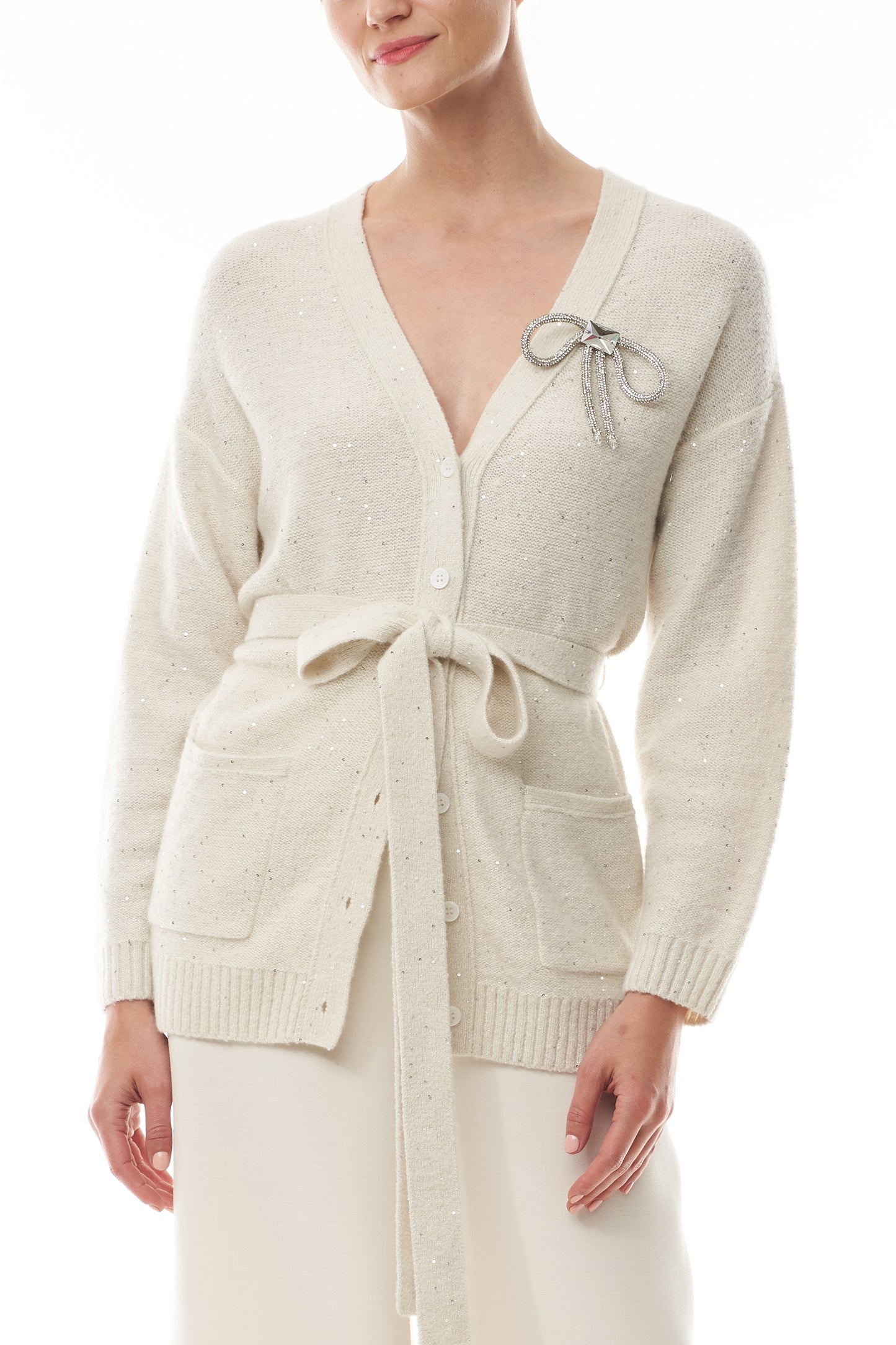 Monique Lhuillier Fall 2025 long sleeve cardigan in ivory sequin cashmere with bow brooch and self-tie belt - front.