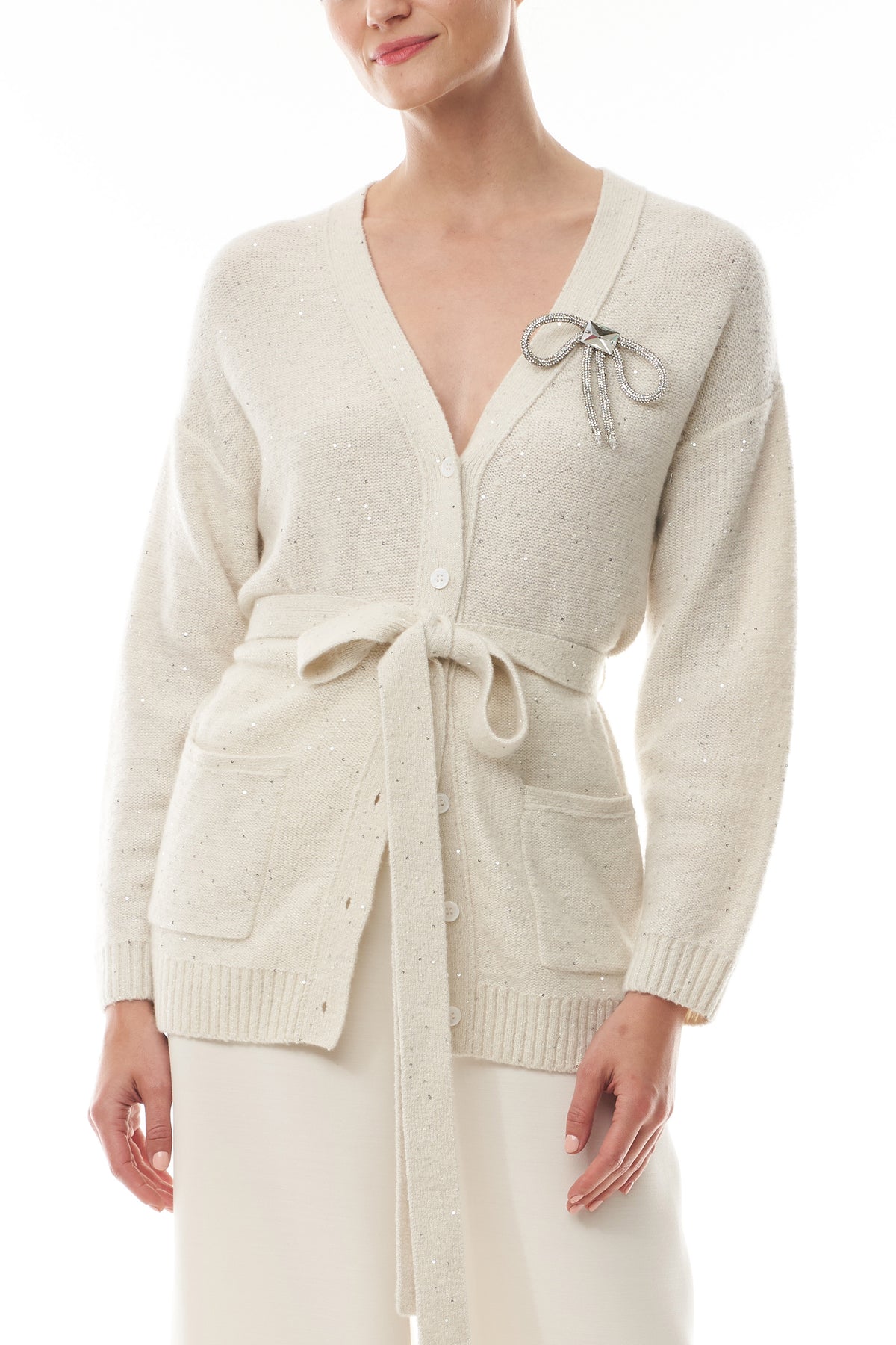 Monique Lhuillier Fall 2025 long sleeve cardigan in ivory sequin cashmere with bow brooch and self-tie belt - front.