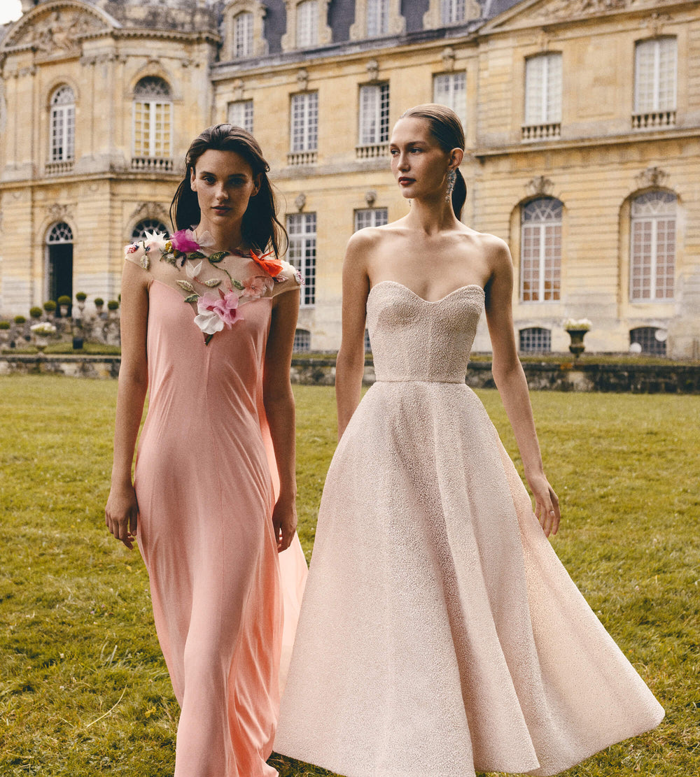 Monique Lhuillier Spring 2024 Melon chiffon caftan gown with floral 3-D embroidery over an illusion tulle neckline next to a powder pink strapless cocktail dress.