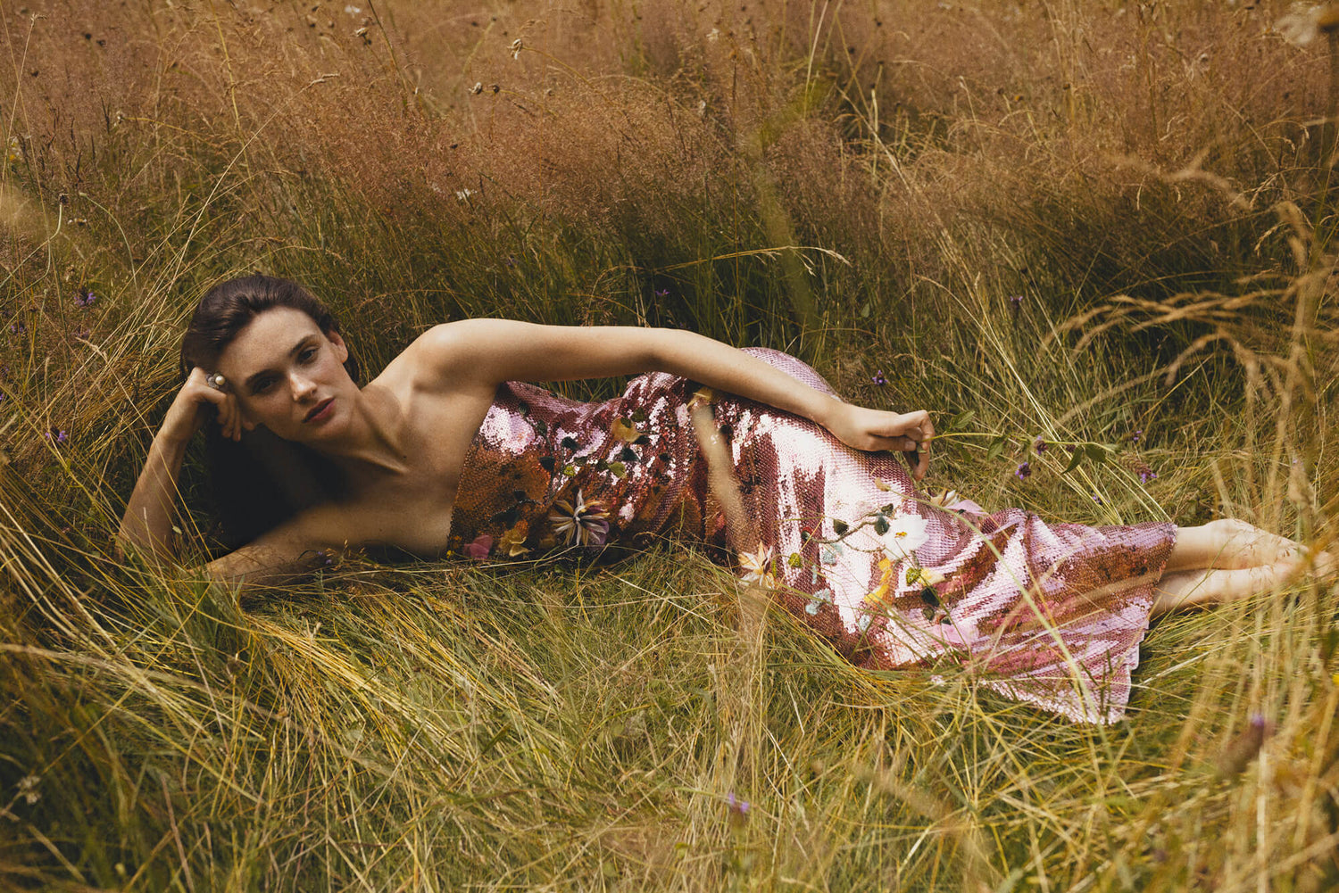 Model in floral sequin column gown laying in the Parisian countryside.