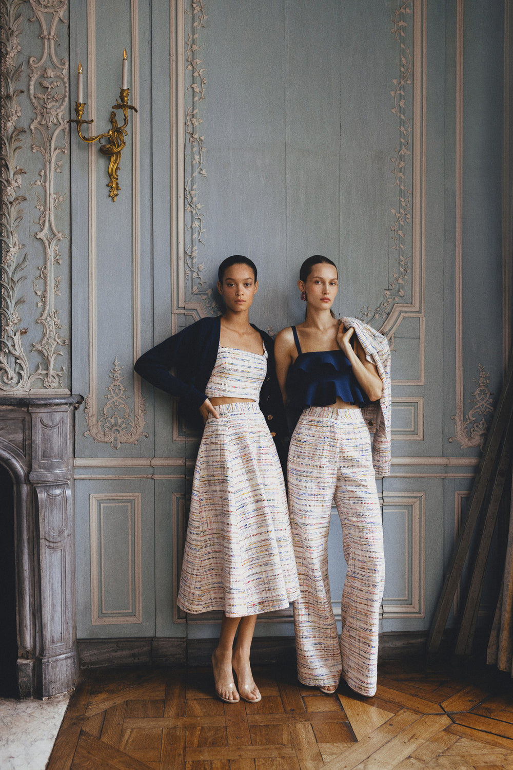 Monique Lhuillier Spring 2024 tweed high waisted trouser and skirt shown with knitwear on two models.