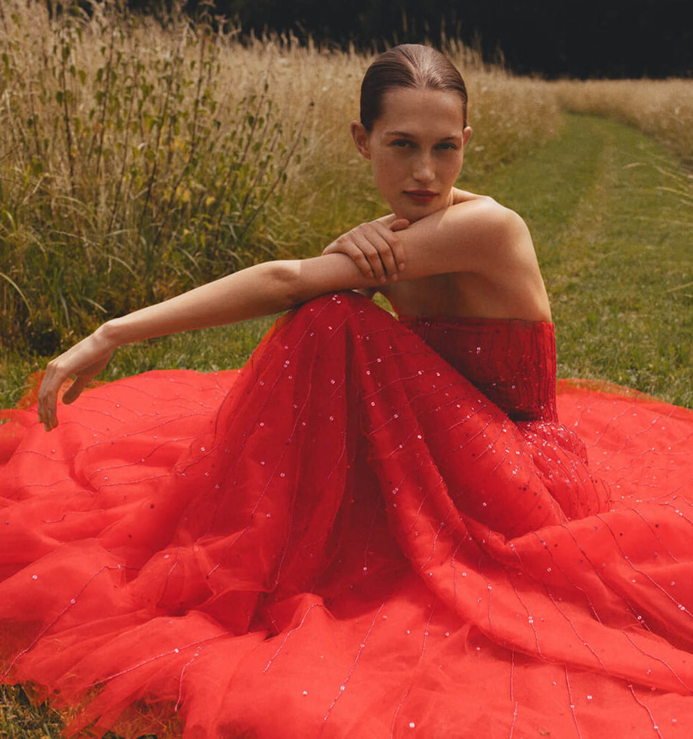 Monique Lhuillier strapless ballgown in cherry red embroidered tulle - model in grass.