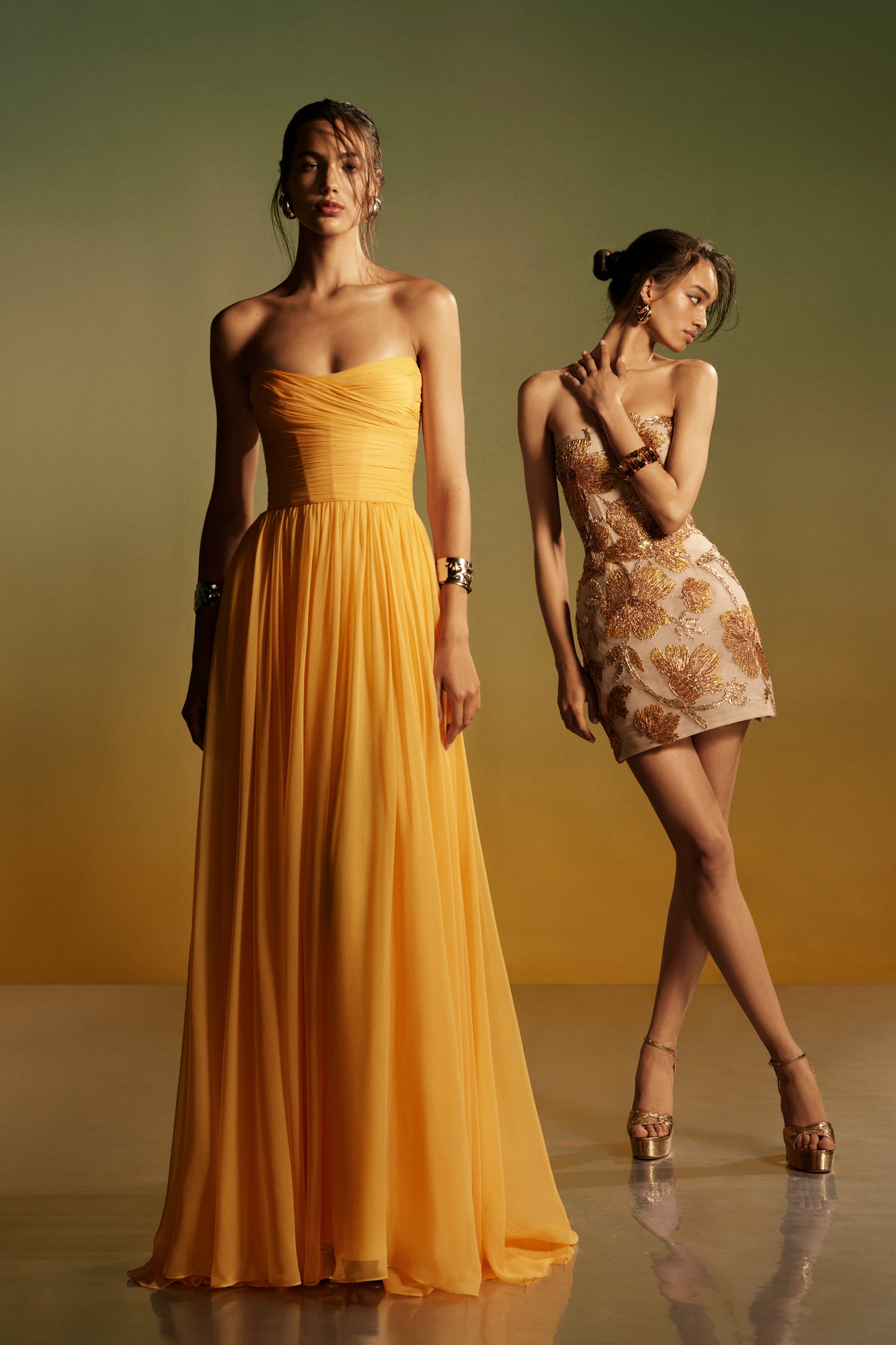 Monique Lhuillier Spring 2026 lookbook image - model on left wearing Mango chiffon strapless gown, model on right wearing gold embroidered mini dress