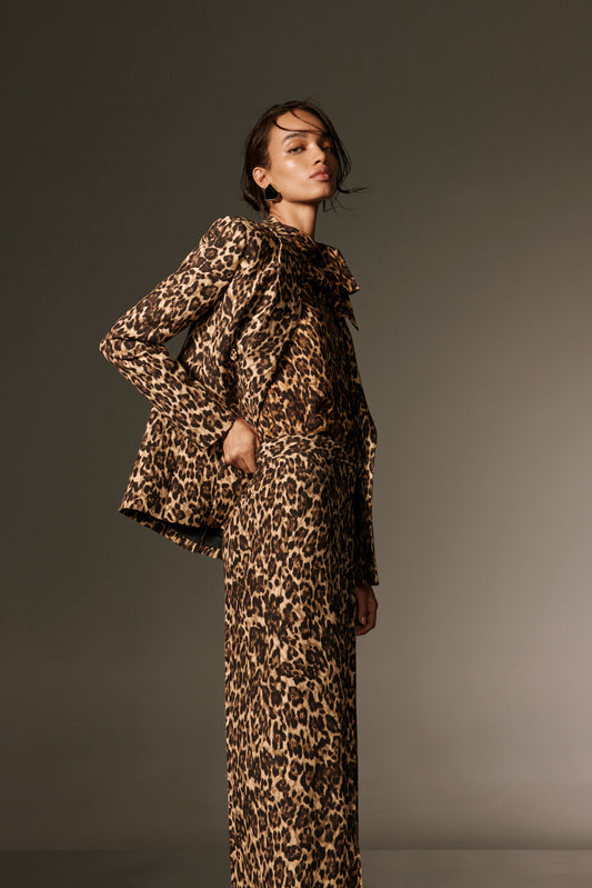 Monique Lhuillier Spring 2026 lookbook image - model wearing leopard georgette scarf neck blouse with leopard suiting straight leg trouser and tuxedo jacket