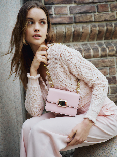 Model wearing blush Monique Lhuillier Fall 2024 Cable Knit Cardigan and trouser with blush Rhea mini shoulder bag with gold chain strap.
