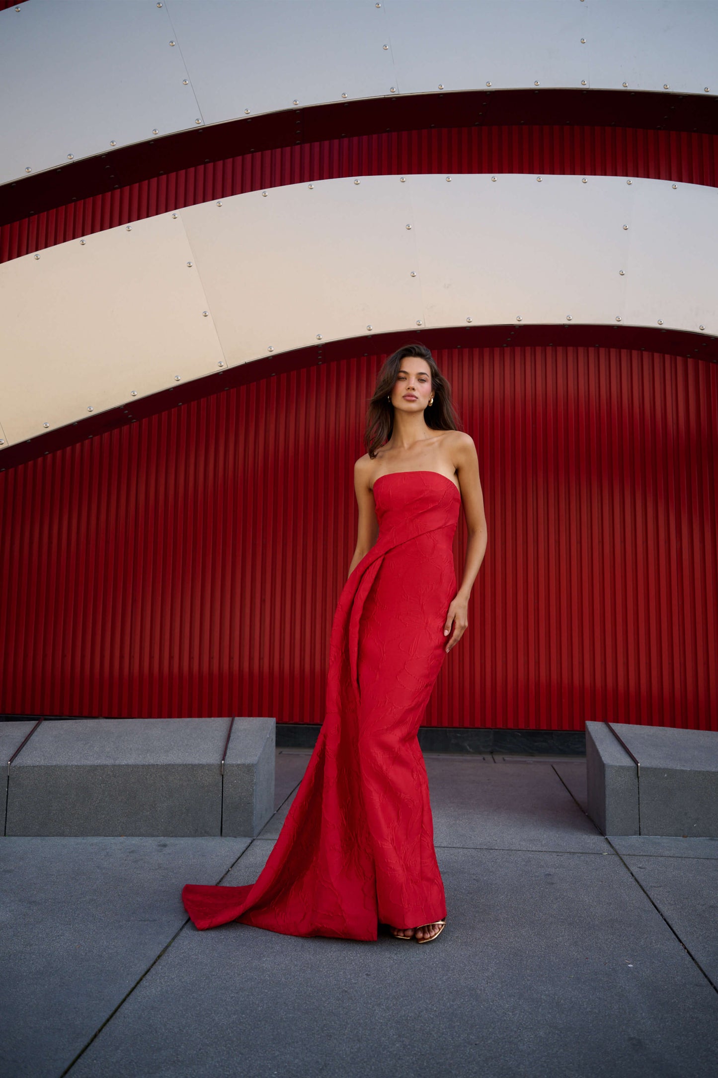 Monique Lhuillier Spring 2026 Poppy Linear Rose Jacquard Strapless Strapless draped column gown with train - model standing on sidewalk.