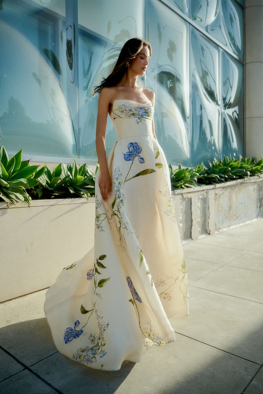 Monique Lhuillier Spring 2026 Ivory Multi Iris Bouquet Printed Gazar Draped bodice
ball gown with front skirt slit - model on sidewalk outside.