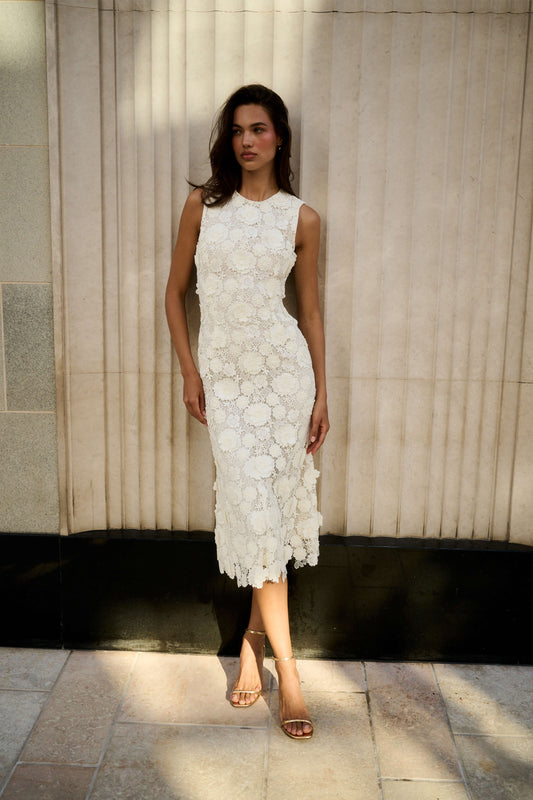 Monique Lhuillier Spring 2026 Ivory Three-dimensional floral lace sleeveless midi dress - model leaning against wall outside.