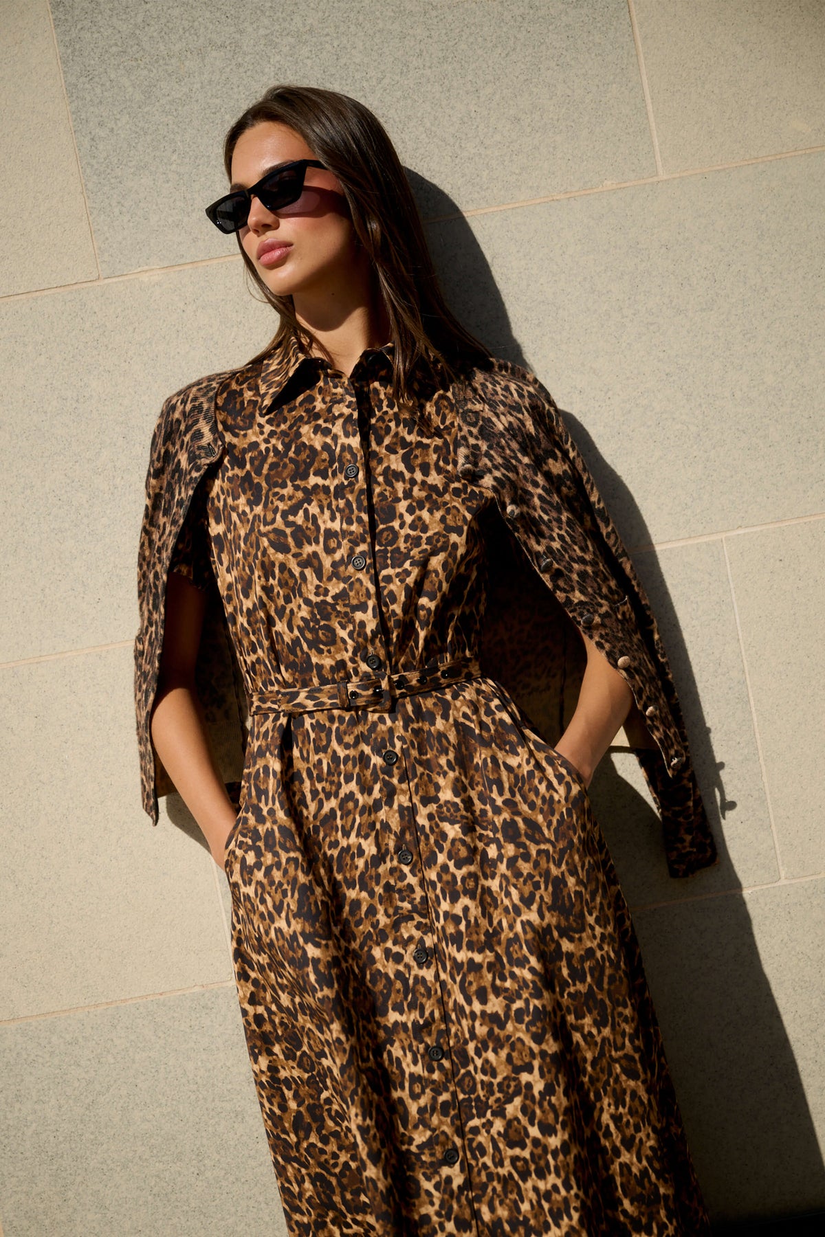 Monique Lhuillier Spring 2026 Leopard Printed Cotton Poplin short sleeve shirt
dress with belt and leopard cashmere cardigan - model leaning on wall outside.