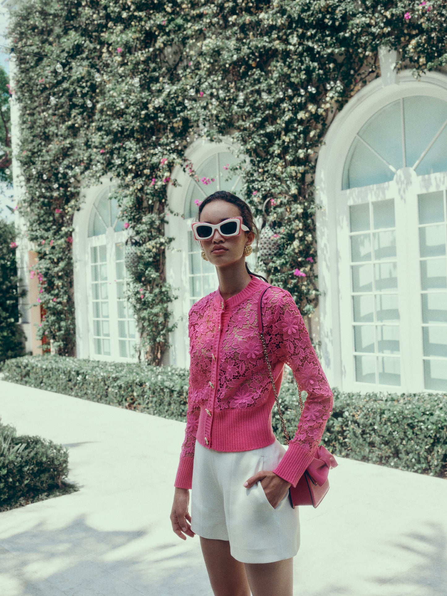 Monique Lhuillier Spring 2025 hibiscus lace cardigan with gold buttons - lookbook photo on model with sunglasses.