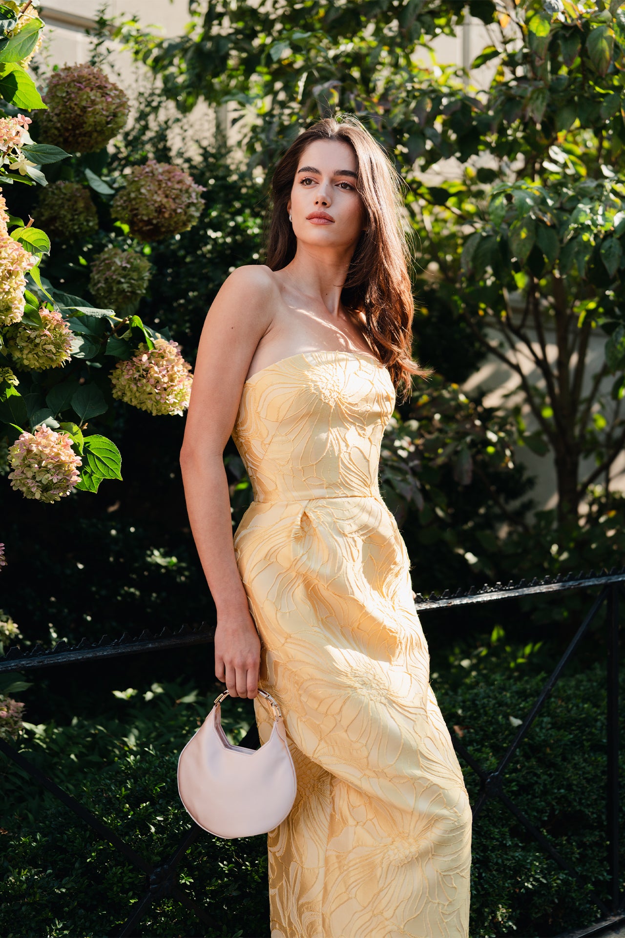 Satin, crescent shaped small evening bag with diamante pale gold metal handle in Blush- on model wearing yellow strapless gown.