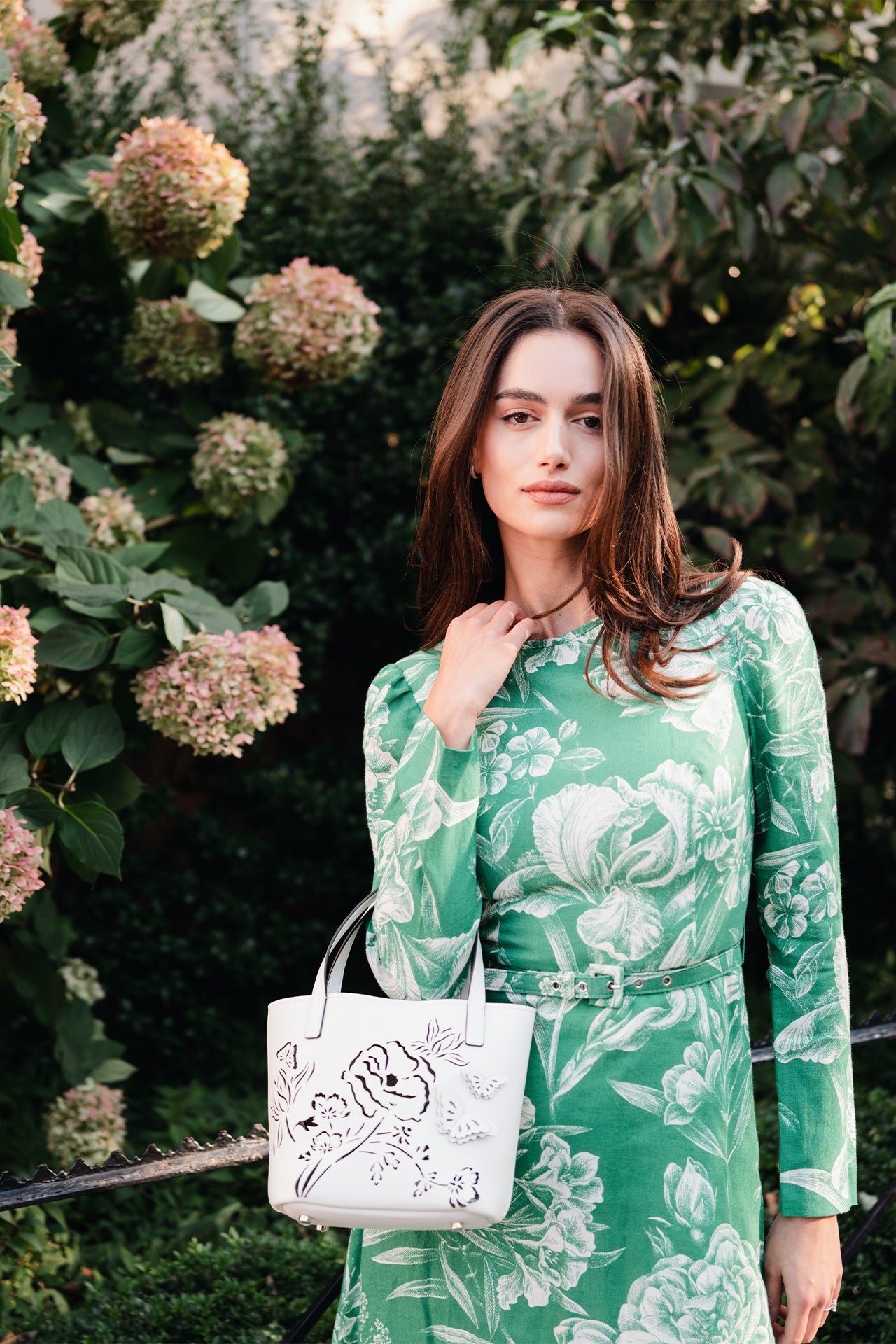 Monique Lhuillier Spring 2025 Floral toile printed linen long sleeve day dress with jewel neckline and circular skirt in grass silk white color - lookbook photo with Colette mini tote.