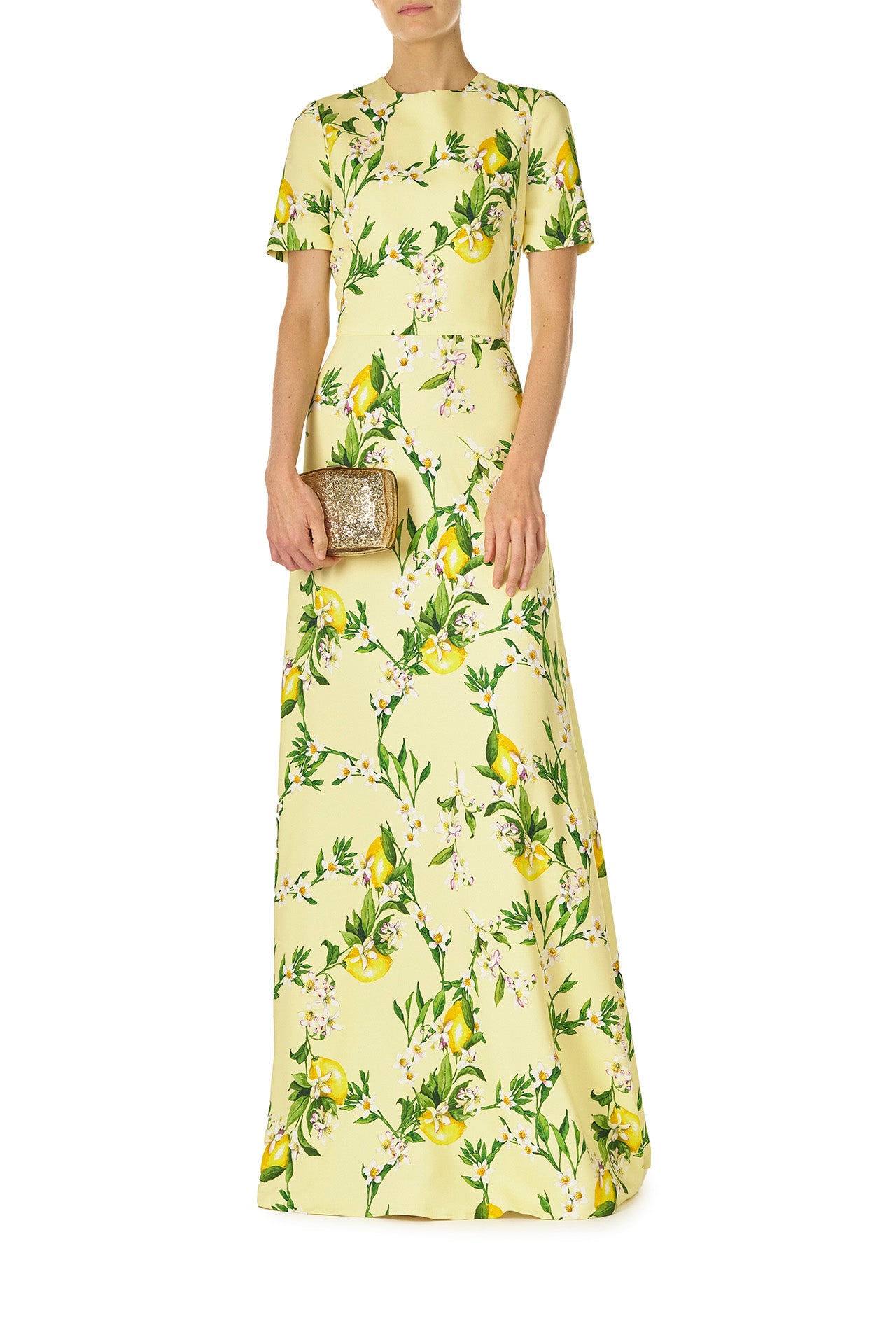 Monique Lhuillier Spring 2025 Short sleeve, floor length gown with jewel neckline in Lemon printed Crepe fabric - front with Dasha clutch in gold.