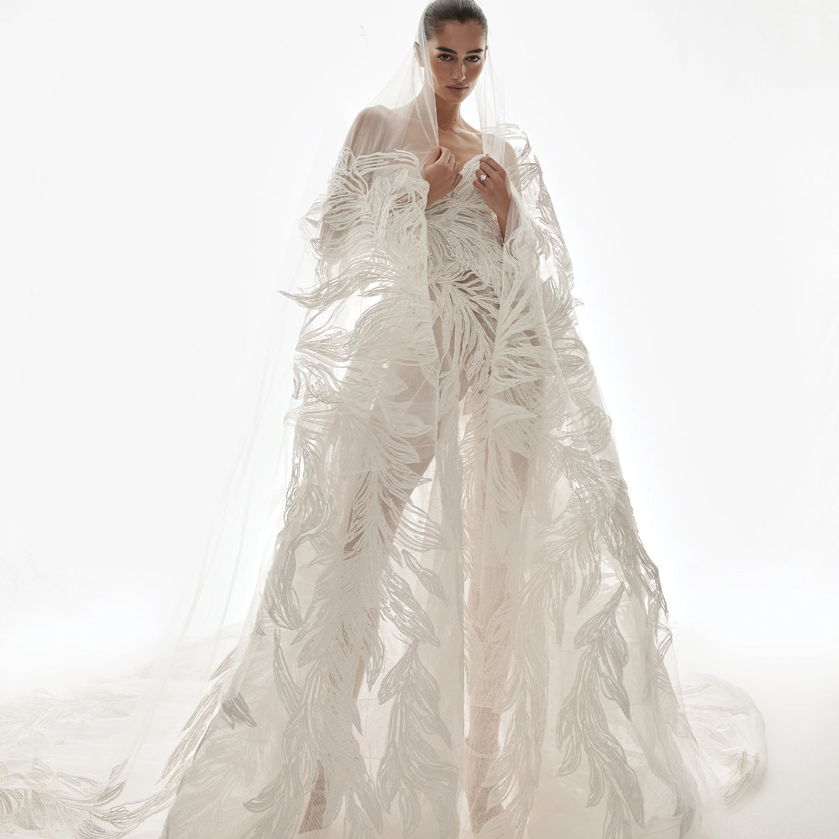 Model wearing Monique Lhuillier Spring 2026 Bridal white Laurel raffia embroidered tulle strapless ball gown with raffia leaf detail with coordinating white two tier Laurel veil with raffia embroidery border