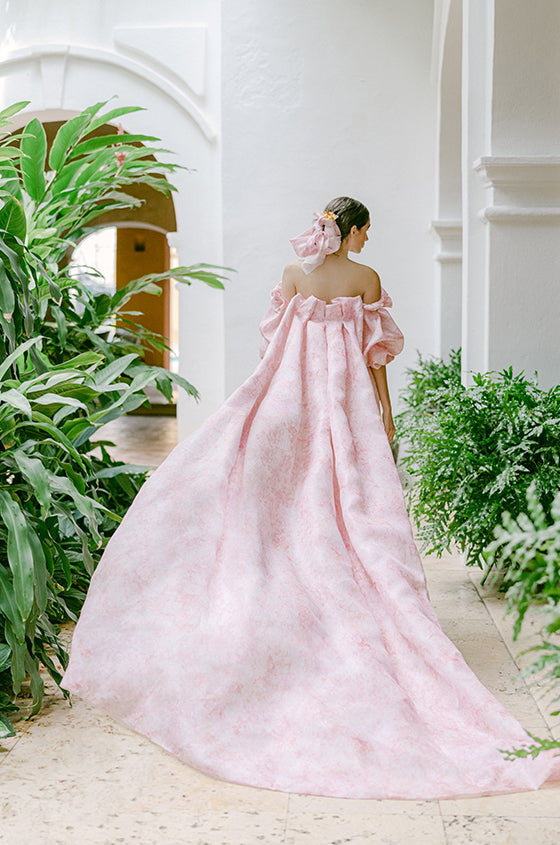 Woman wearing Monique Lhuillier Fall 2022 pink floral Petal cocktail dress with puff sleeve and long matching Petal cape