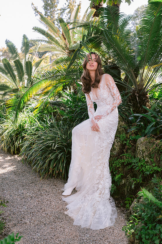 Woman wearing Monique Lhuillier Spring 2024 white lace embroidered V-neck modified a-line Ivy gown with embroidered long-sleeve Ivy jacket