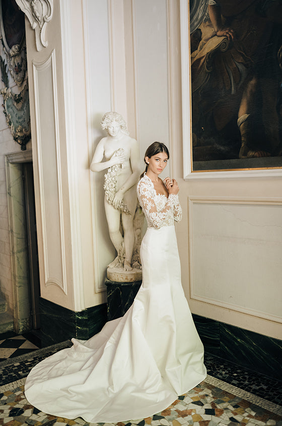 Woman wearing Monique Lhuillier Fall 2020 white strapless fitted India gown with lace bodice and duchess satin skirt and lace bolero