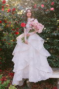 Woman wearing Monique Lhuillier Spring 2024 white lace Papillon tiered ballgown with matching high-neck long sleeve jacket