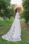 Woman wearing Monique Lhuillier Spring 2024 white strapless lace corseted Eden slip gown with matching long sleeve lace cape