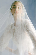 Woman wearing Monique Lhuillier Fall 2022 long sleeve white beaded sheath Emma gown with sheer veil over face