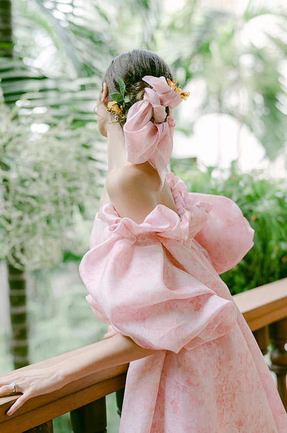 Model leaning on railing in blush floral printed Petal puff sleeve dress with matching Petal cape