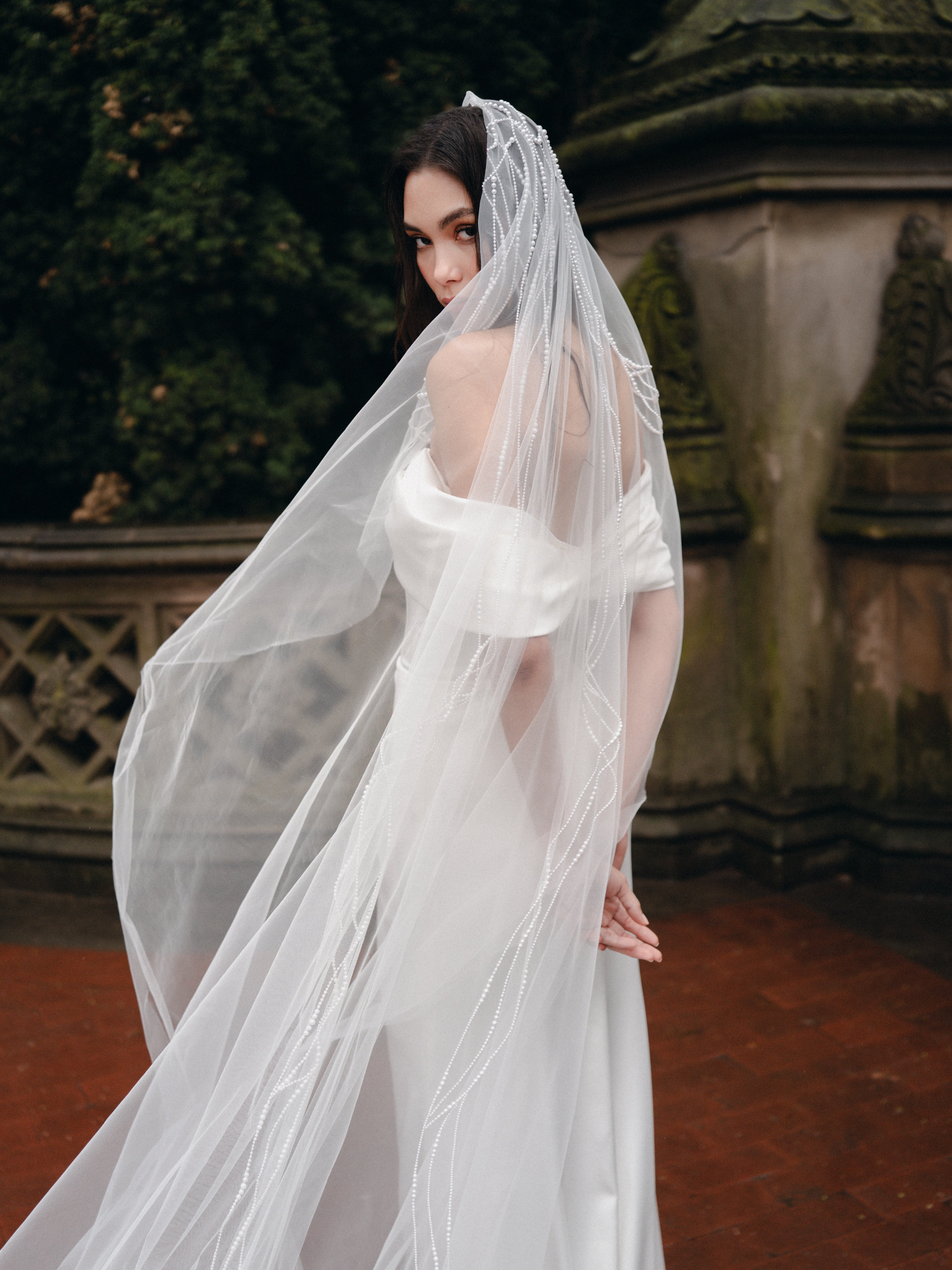 Crepe Satin draped off-the-shoulder gown paired with with pearl & bow detailed veil.