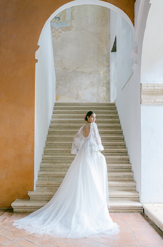 Woman wearing Monique Lhuillier Fall 2022 white tulle and lace scoop back Valentina ballgown with billowed sleeve and long train