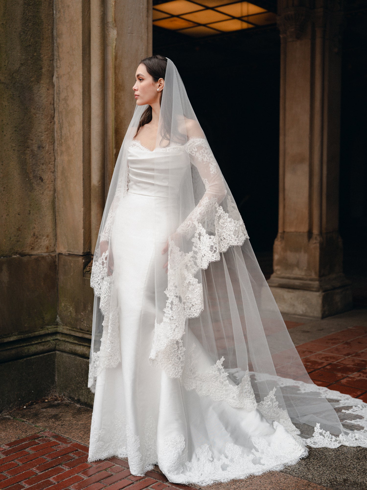 Mikado trumpet gown with draped bodice, lace sleeves and lace hem border. Paired with the Cathedral length, two tier lace trimmed veil.