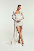 Monique Lhuillier Spring 2027 Bridal two-piece Revel strapless corset bodice and mini skirt in ivory French re-embroidered lace with long sleeve peplum overcoat with split train.