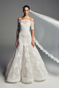 Monique Lhuillier Spring 2027 Bridal Strapless corseted Cherish trumpet gown with coned skirt in silk white re-embroidered lace with off-the-shoulder elbow length sleeve jacket and Mantilla style tulle and scallop re-embroidered lace veil.