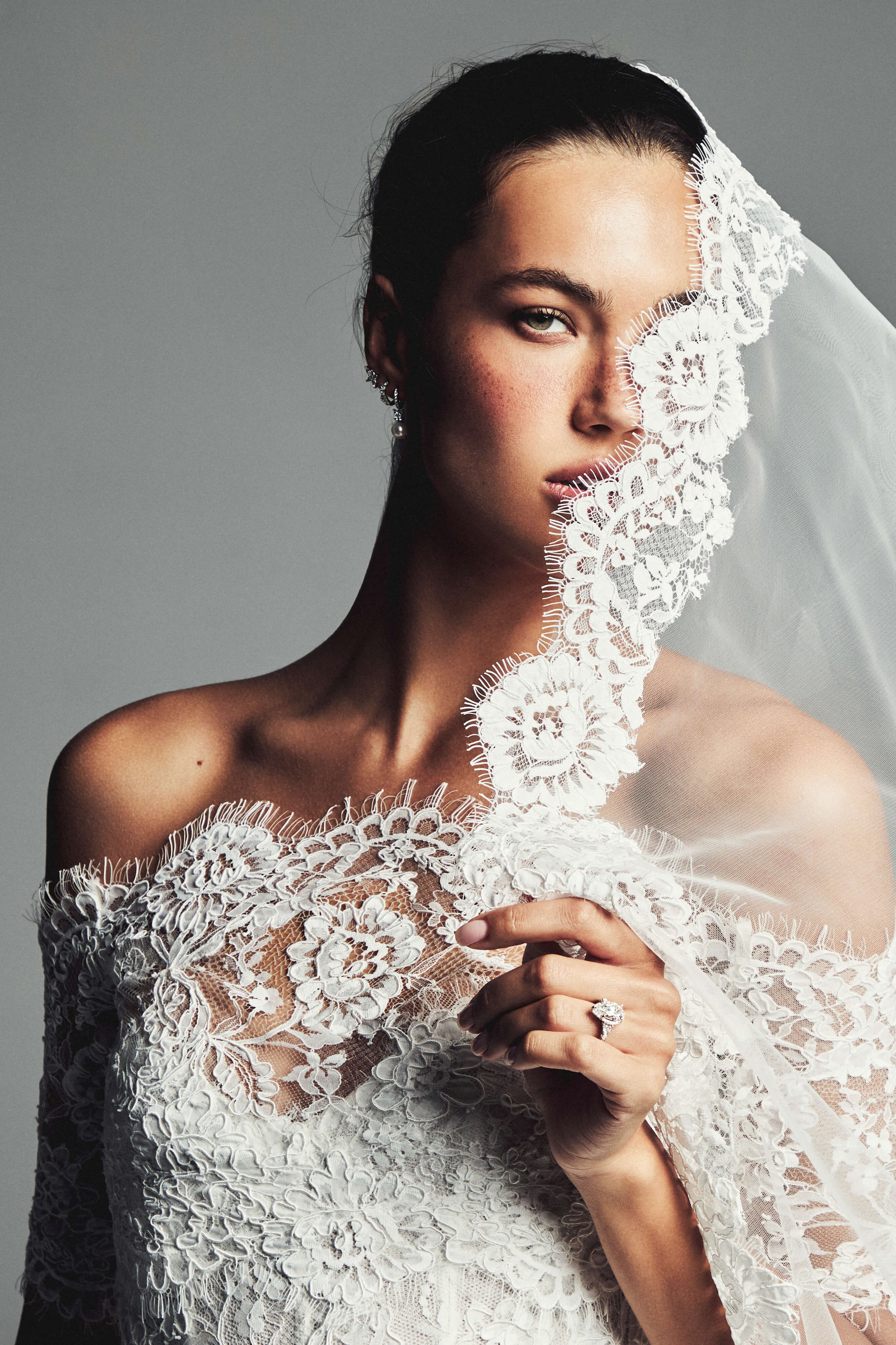 Monique Lhuillier Spring 2027 Bridal Strapless corseted trumpet Cherish gown with coned skirt in silk white re-embroidered lace with off-the-shoulder elbow length sleeve jacket and Mantilla style tulle and scallop re-embroidered lace veil.