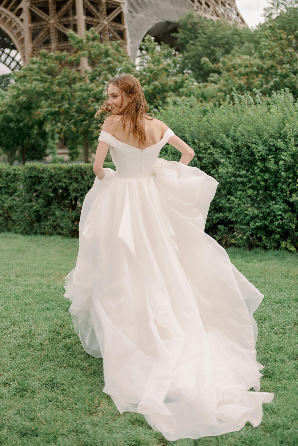 Woman wearing Monique Lhuillier Spring 2024 Bliss white organza off-the-shoulder draped bodice BL24102 ballgown
