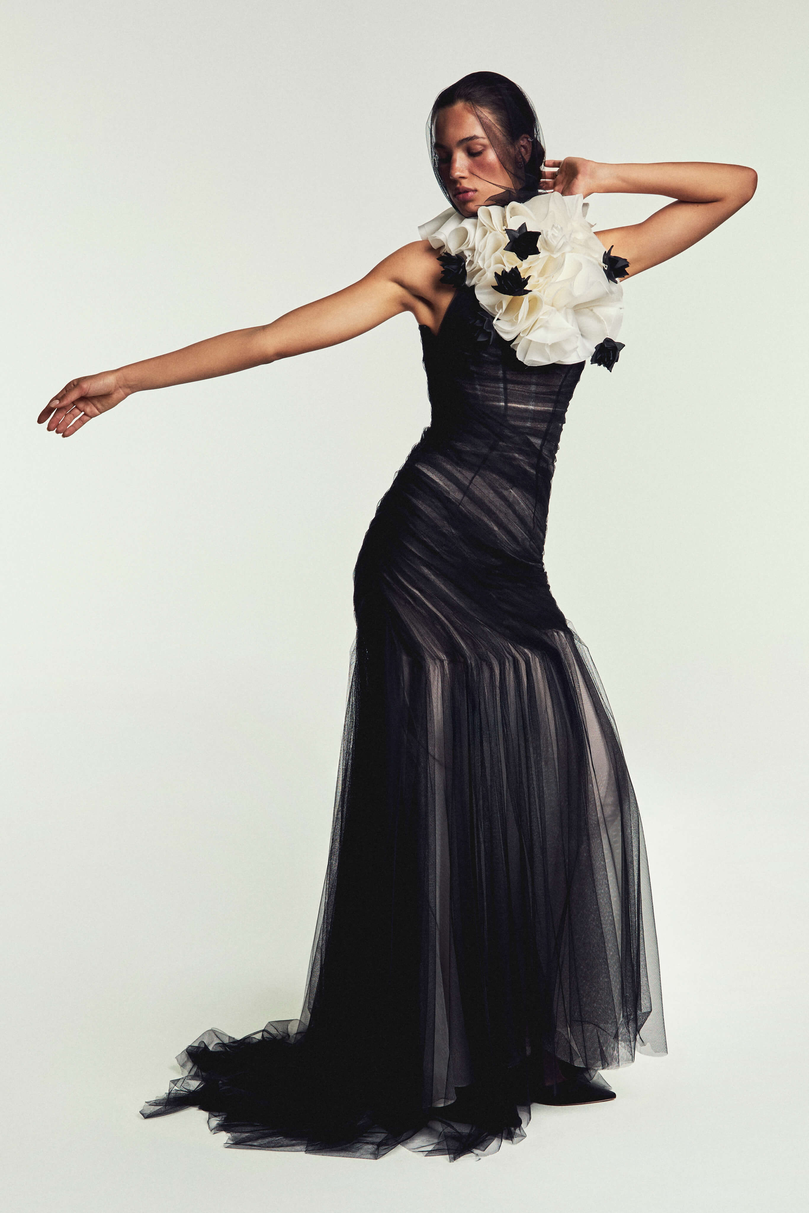 Monique Lhuillier Spring 2027 Bridal Hand draped Raven trumpet gown with halter neckline in noir and silk white Spanish tulle and ruffled neck collar with floral detail in silk white and noir satin faced organza.
