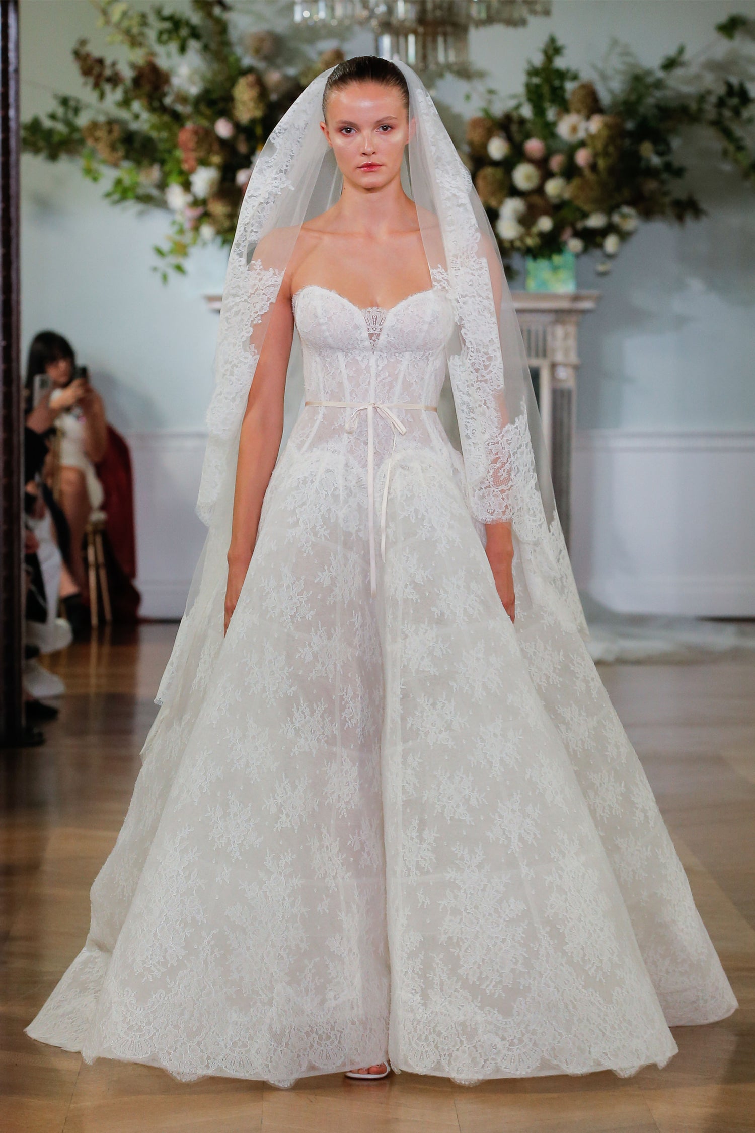 Monique Lhuillier Fall 2026 Bridal ivory chantilly lace strapless drop waist Odette ballgown with ribbon at waist and lace-trim Odette veil - runway.