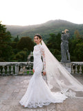 Woman wearing Monique Lhuillier Fall 2024 white lace fitted long sleeve high neck Starlet sheath gown with lace and tulle veil