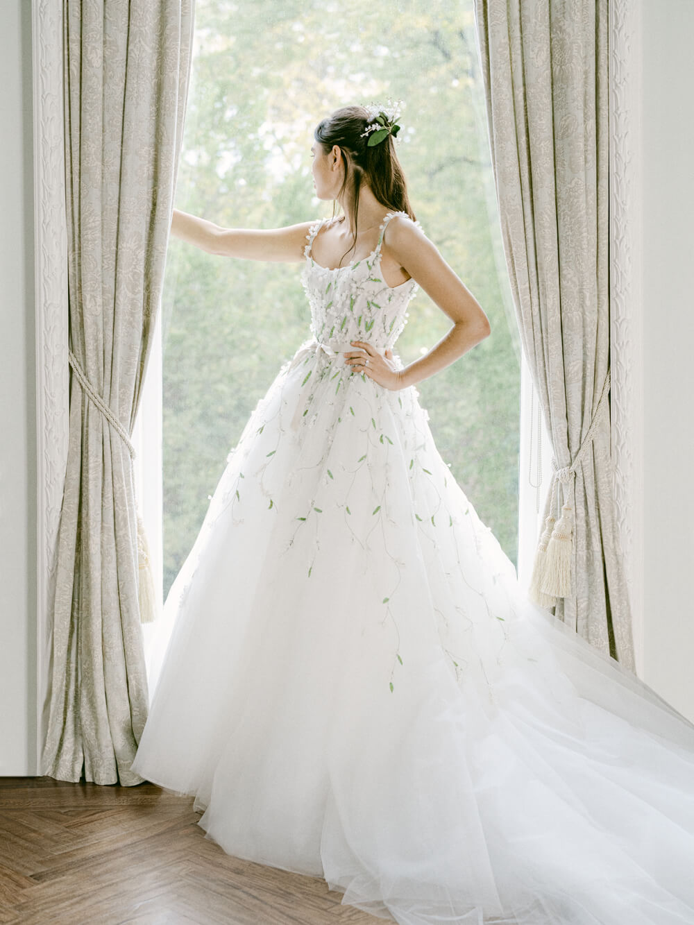 Woman in window wearing white Monique Lhuillier Fall 2021 Lily of the Valley tulle ball gown with green 3-D embroidery