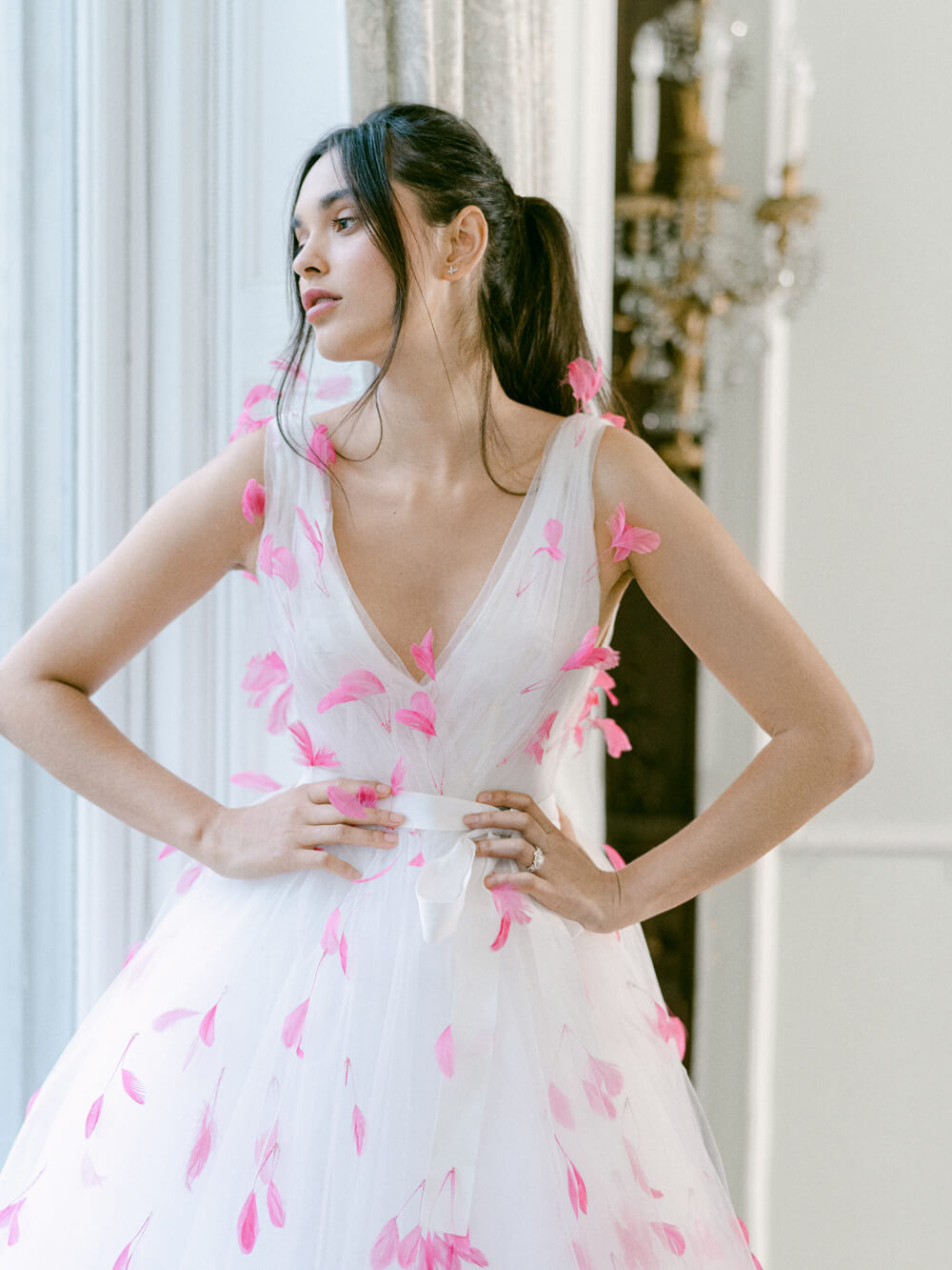 Woman wearing white Monique Lhuillier Fall 2021 tulle v-neck a-line gown with bright pink feather applique