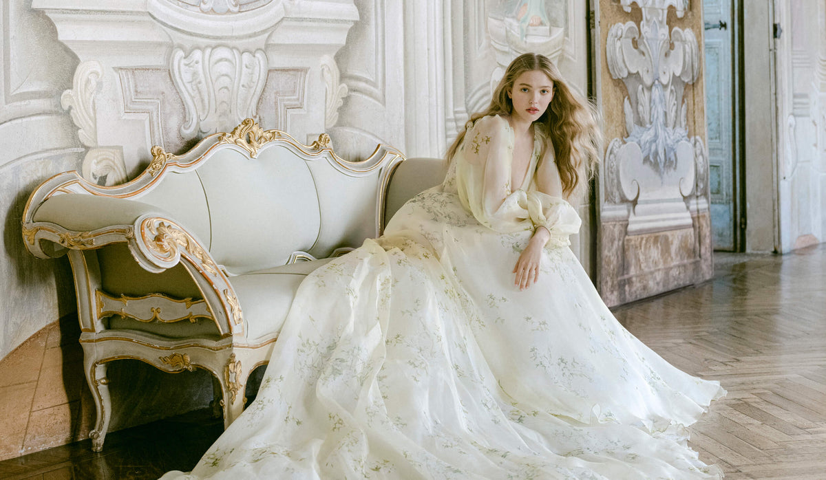 Woman sitting in yellow and green floral print Monique Lhuillier Spring 2022 Buttercup a-line gown with billow sleeves and long train