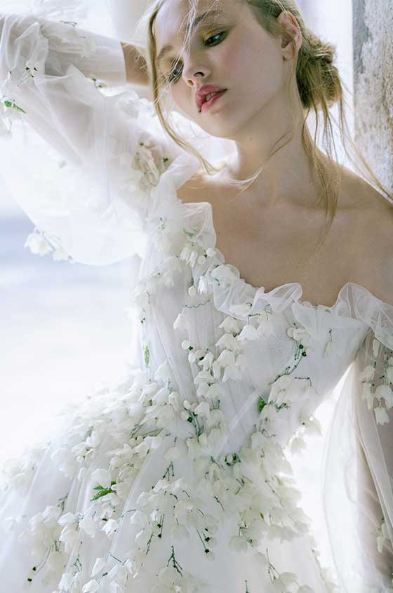 Model in doorway wearing white off-the-shoulder Freesia gown with billow sleeve and green 3D floral embroidery
