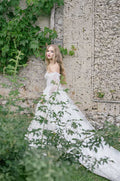 Woman wearing Monique Lhuillier Spring 2022 white embroidered a-line Splendid gown with off-the-shoulder billowed sleeve
