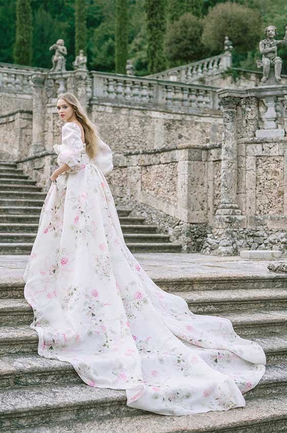 Woman wearing Monique Lhuillier Spring 2022 white, blush and green floral printed Dahlia ballgown with billowed sleeve and long train