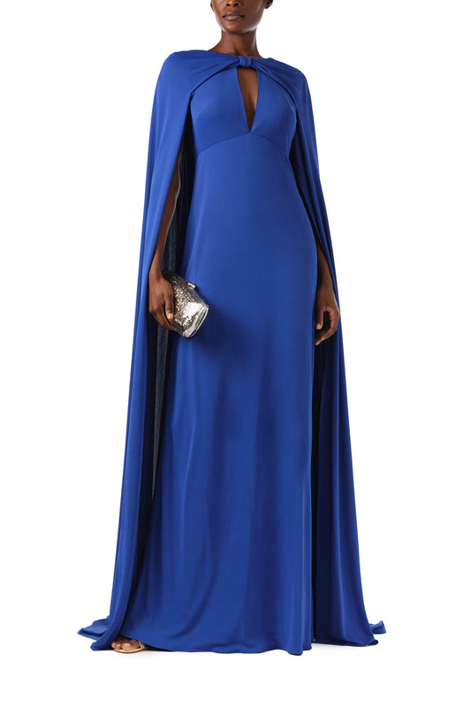 Monique Lhuillier Spring 2024 royal blue crepe-back satin gown with attached cape and keyhole bodice - front with Viv handbag.