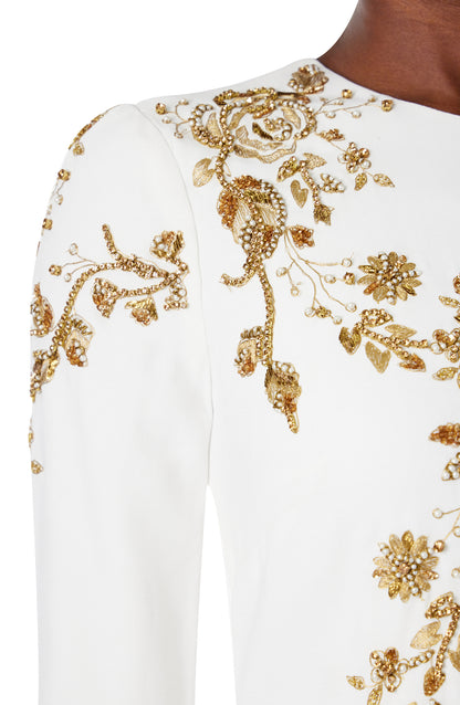 Monique Lhuillier silk white jewel neck, long sleeve column gown with gold embroidery.