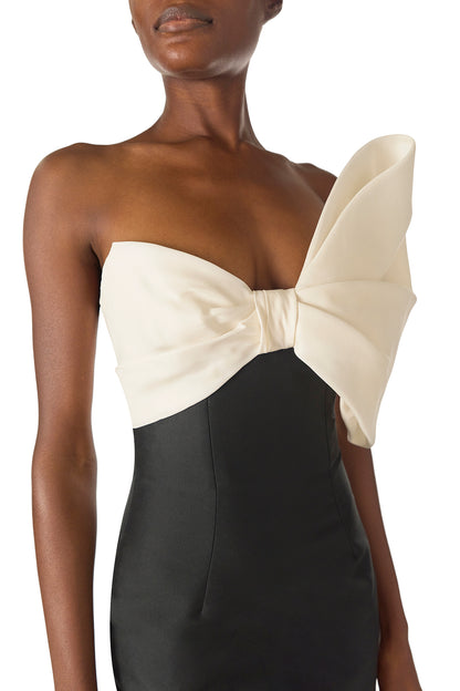 Monique Lhuillier Spring 2025 Strapless column gown with asymmetric draped bow neckline and pleated back train in Noir + Silk White Mikado - bow neckline.