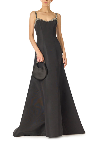 Monique Lhuillier Spring 2025 Modified trumpet gown with crystal beaded neckline and spaghetti straps in Noir Silk Faille - front with Demi handbag.