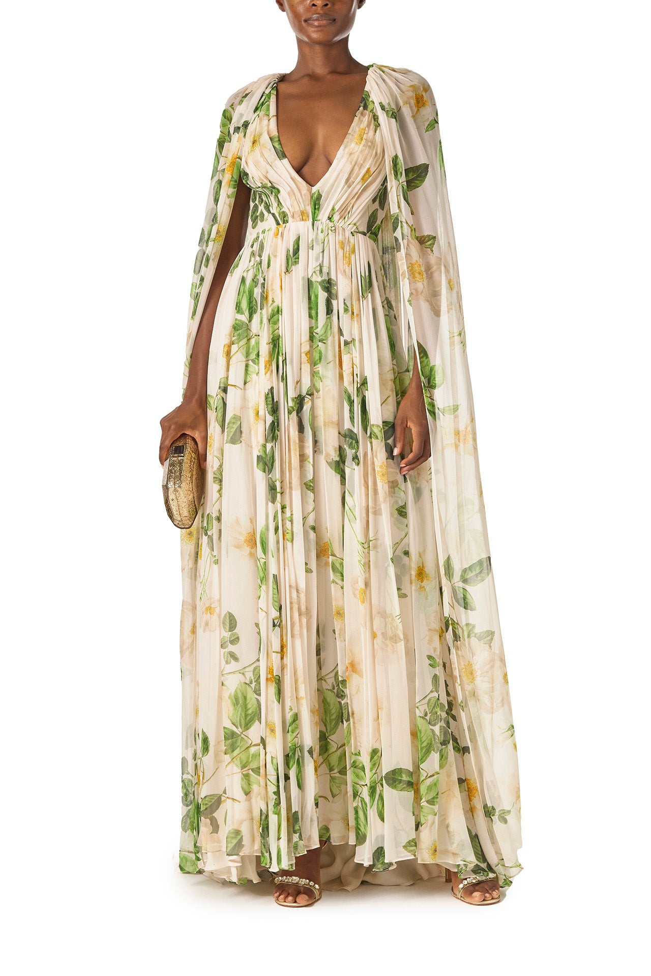 Monique Lhuillier Spring 2025 Draped, v-neck gown in Rose Printed Chiffon with low back and flowing, integral cape - front with gold handbag.