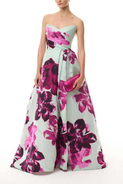 Monique Lhuillier Fall 2025 strapless ballgown with high leg slit and pockets in electric floral printed gazar - front with Viv clutch.